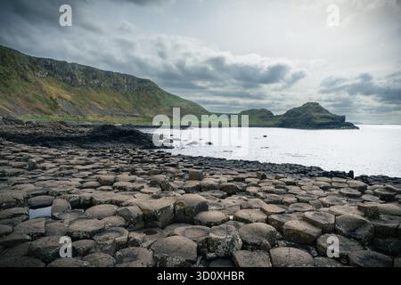 Blick auf den Giant's Causeway in Nordirland, aufgenommen an einem bewölkten späten Nachmittag, mit sechseckigen Basaltsäulen im Vordergrund und Bergen A Stockfoto