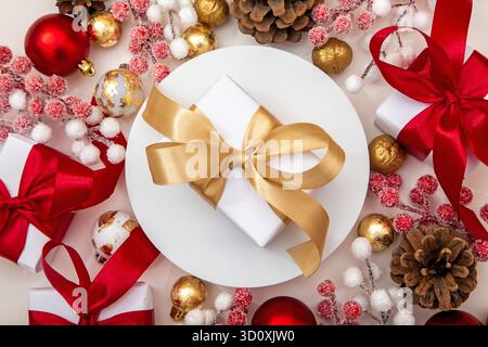 Elegantes Geschenk mit goldenem Band, umgeben von roten und weißen Ornamenten. Luxus-Urlaubshintergrund für Werbung und Grußkartendesign. Stockfoto