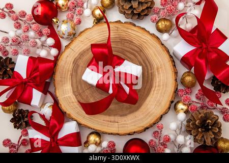 Weißes Geschenk mit goldener Schleife, umgeben von roten und weißen Weihnachtsschmuck, Tannenzapfen und Beeren. Festliche Komposition zu Weihnachten und Neujahr Stockfoto