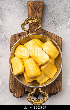 Süße, goldene Jackfrucht-Schoten (Zwiebeln) in einer traditionellen Metallschale mit Gabel. Exotischer tropischer Snack oder Dessert mit Kopierraum. Stockfoto