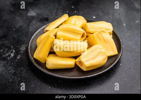 Süße, goldgelbe Jackfruchengruten (Zwiebeln), serviert auf einem schwarzen Teller auf dunklem Steinhintergrund. Exotische tropische Früchte mit Kopierraum. Stockfoto