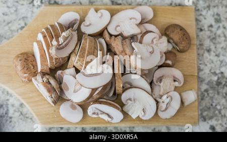Frische Pilze werden in Scheiben geschnitten und ordentlich auf einem hölzernen Schneidebrett auf einer hellen Arbeitsplatte angeordnet. Ideal zum Kochen oder Garnieren in verschiedenen Sorten Stockfoto