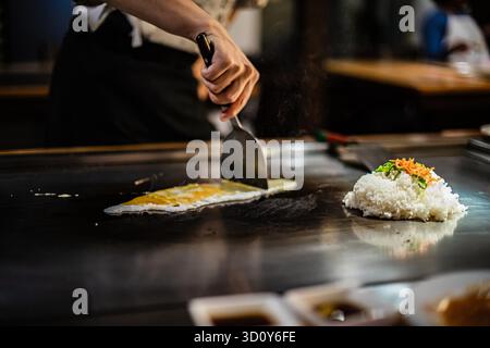 Teppanyaki, japanische Teppanshow in traditionellem Restaurant. Hände des Kochs. Der Koch bereitet Fleisch, Fisch, Reis und Gemüse auf einem heißen Tisch vor den Gästen zu. Küche Völker der Welt Konzept Stockfoto