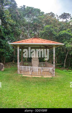 Eine Steinstatue unter einem Pavillon im archäologischen Park von San Agustin, Kolumbien, umgeben von üppigem Grün. Stockfoto