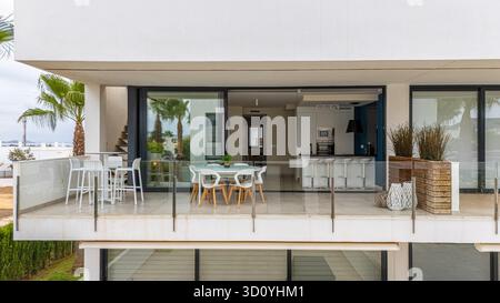 Modernes Apartment im ersten Stock mit stilvollem Balkon mit Essgarnitur im Freien und Barsitzen. Der Raum ist direkt mit einer offenen Küche verbunden Stockfoto