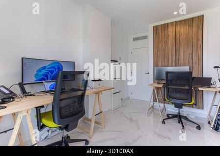 Funktionales Home Office mit zwei Arbeitsplätzen, Holzmöbeln, ergonomischen Stühlen und großen Bildschirmen in einem sauberen, modernen Raum. Stockfoto