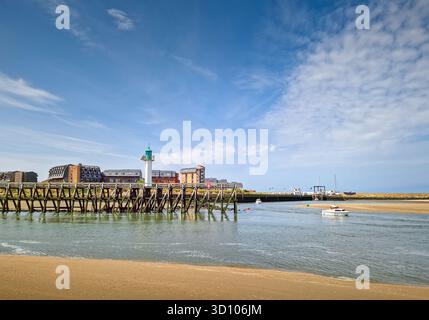 Heller, sonniger Blick auf die Hafeneinfahrt in Trouville-sur-Mer, Frankreich. Sandstrand trifft auf einen Gezeitenfluss, der zum Meer fließt. Ein Leuchtturm und ein paar s Stockfoto