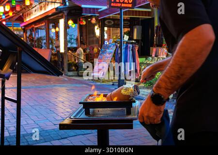 Der Kellner bereitet türkisches Testi Kebab-Töpferkebab, herzhaftes Fleisch und Gemüse zu, das über einer Flamme in einem Tontopf in einer bunten Straße, Istanbul Türkei, gekocht wird Stockfoto