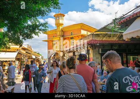 Fußgänger spazieren durch die historische mittelalterliche Altstadt mit der Mehmet-Aga-Moschee in der Ferne, in Rhodos, Griechenland. Stockfoto