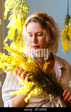 Russland, Moskau, 25.07.2024 Frau, die drinnen einen zarten Haufen gelber Mimosa-Blumen hält. Wunderschöner Blumenstrauß im Frühling mit blühendem Sonnenschein. Stockfoto