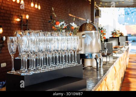 Glänzende Glaswaren, die neben einer Thermokaraffe im rustikalen Ziegel- und Blumendekor angeordnet sind - ideal für gehobene Gastronomie oder luxuriöse Markenbezeichnungen. Stockfoto