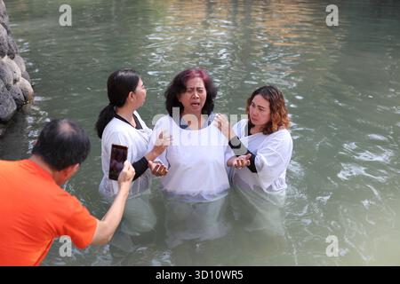 Yardenit Taufstätte, protestantische indonesische Frau in einem weißen Kleid steht im Jordan und betet, bevor sie von zwei Frauen getauft wird, eine davon ein Pastor. Stockfoto