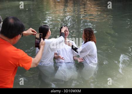 Yardenit Taufstätte, protestantische indonesische Frau, die ein weißes Kleid trägt, wird von einem Pastor gehalten, der im Jordan von zwei Frauen getauft wird. Stockfoto