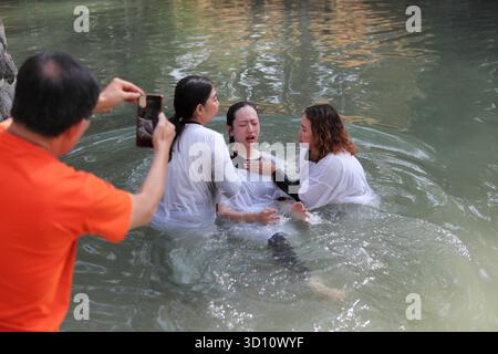Yardenit Taufstätte, protestantische indonesische Frau trägt ein weißes Kleid und kommt aus dem Wasser, nachdem sie im Jordan von zwei Frauen getauft wurde, eine ein Pastor. Stockfoto