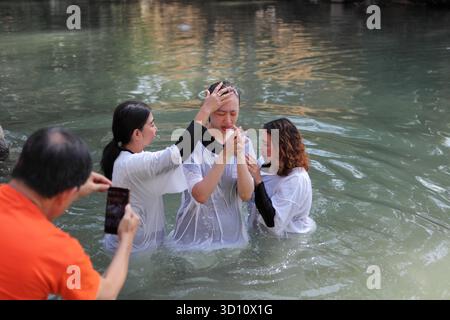 Yardenit Taufstätte, protestantische indonesische Frau trägt ein weißes Kleid und kommt aus dem Wasser, nachdem sie im Jordan von zwei Frauen getauft wurde, eine ein Pastor. Stockfoto