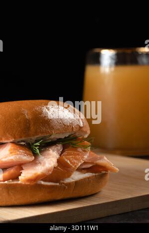 Ein Sandwich mit Lachs und Dill sitzt auf einem hölzernen Schneidebrett neben einem Glas Saft Stockfoto
