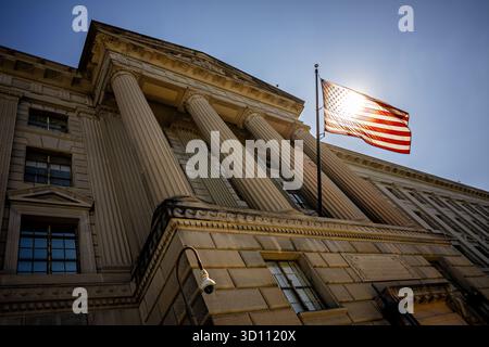 US-Flagge von Sun am Herbert C Hoover Federal Building Washington DC / WASHINGTON DC – die US-Flagge wird von der Sonne vor der Fassade des Herbert C. Hoover Building, dem Hauptquartier des US-Handelsministeriums, beleuchtet. Das monumentale neoklassizistische Bauwerk, das 1932 fertiggestellt wurde, nimmt eine herausragende Position im Federal Triangle entlang der Pennsylvania Avenue NW ein. Benannt wurde es nach Herbert C. Hoover, der vor seiner Präsidentschaft als 31. Präsident der Vereinigten Staaten und als Handelsminister fungierte. Stockfoto