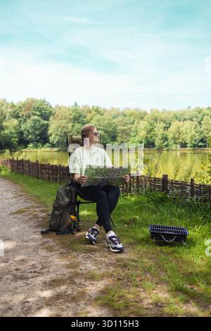 Frau, die im Naturpark auf Campingstuhl mit Laptop sitzt Stockfoto