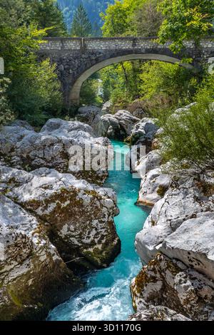 Der türkisfarbene Fluss soca fließt schnell durch die kleine Soca-Schlucht in Bovec, Slowenien. Eine Steinbrücke überspannt die Schlucht über dem rauschenden Wasser. Stockfoto