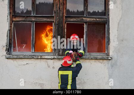 Feuerwehrmann, der ein Baby aus dem brennenden Gebäude rettet, Feuerwehrmann in Aktion Kind retten, Notfallsituation, Feuer im Haus, Gefahr, Rettungsaktion Stockfoto