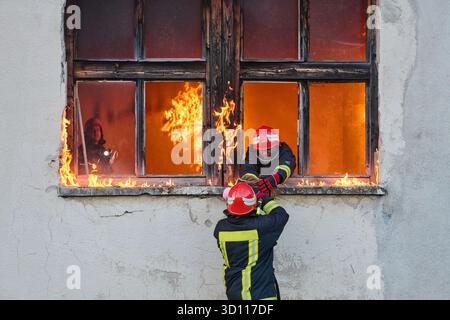 Feuerwehrmann, der ein Baby aus dem brennenden Gebäude rettet, Feuerwehrmann in Aktion Kind retten, Notfallsituation, Feuer im Haus, Gefahr, Rettungsaktion Stockfoto