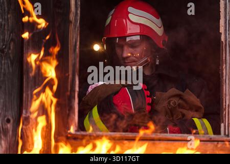 Feuerwehrmann, der ein Baby aus dem brennenden Gebäude rettet, Feuerwehrmann in Aktion Kind retten, Notfallsituation, Feuer im Haus, Gefahr, Rettungsaktion Stockfoto