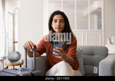 Ernsthafte junge hispanische Reiserin, die im Hotelzimmer sitzt Stockfoto
