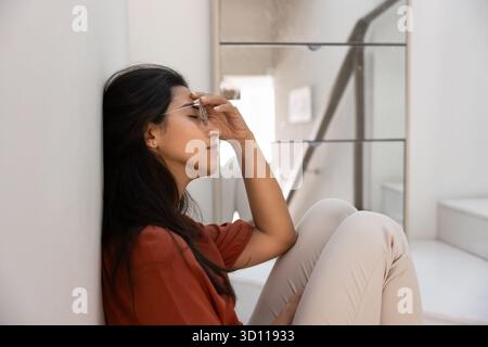 Müde gestresste junge hispanische Frau in Brille, die auf dem Boden sitzt Stockfoto