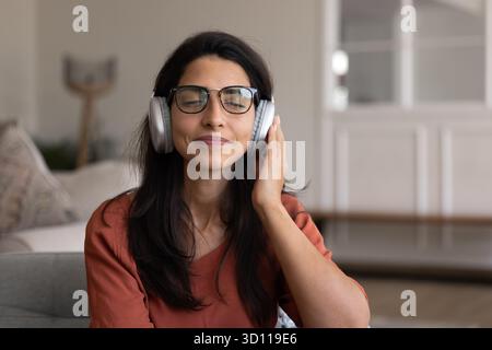 Positive friedliche hispanische Frau im Kopfhörer, die sich zu Hause entspannt Stockfoto