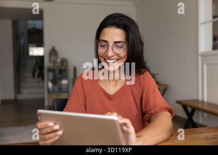 Glückliche schöne hispanische Frau in eleganter Brille, die im Internet surft Stockfoto