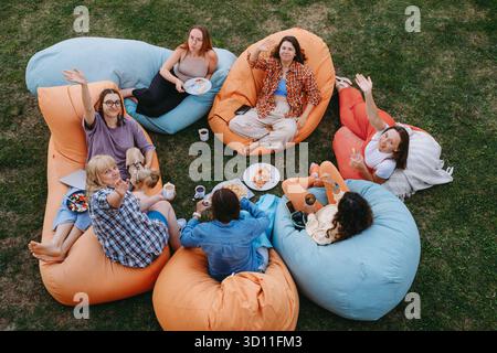 Freunde, die sich auf bunten Sitzsäcken im Freien entspannen und Essen und Getränke in zwangloser geselliger Atmosphäre mit einem kleinen Hund teilen. Frau informell Stockfoto