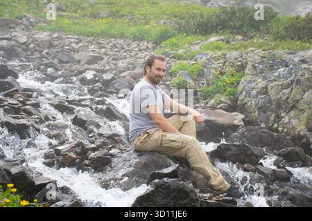 Mann, der auf einem Felsen auf einem Berg sitzt, in einer nebeligen Umgebung. Stockfoto