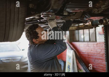 Ein Mechaniker konzentriert sich auf die Reparatur eines Fahrzeugs mit seinen Werkzeugen in der Hand. Die Umgebung ist eine Garage mit Visi Stockfoto