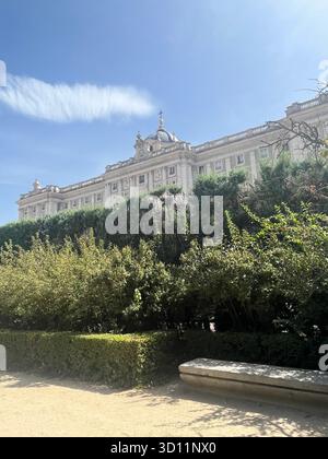 Seitenansicht des Königlichen Palastes von Madrid von Jardines de Sabatini an einem sonnigen Sommertag mit blauem Himmel, Bäumen, Gartenbank und einer wunderschönen Wolke. Stockfoto