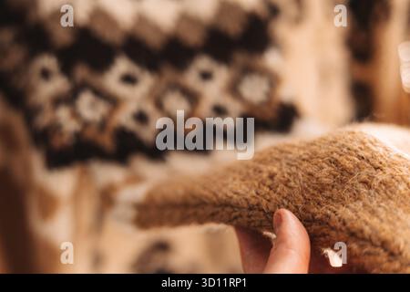 Nahaufnahme einer Hand mit einem weichen, strukturierten braunen und beigefarbenen Pullover. Die Hand hält sanft einen Teil eines gemütlichen, warmen Pullovers und zeigt ihn Stockfoto