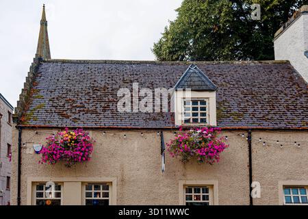 INVERNESS, SCHOTTLAND – 21. August 2024: Moosbedecktes Dach und lebendige Blumenkörbe schmücken ein traditionelles Steinhaus im historischen Herzen von Inverne Stockfoto