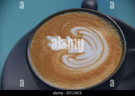 Eine extreme Nahaufnahme eines Cappuccino-Kaffees mit einem sehr schicken Design im Obermaterial. Schwarze Töpfertasse und Untertasse. Stockfoto