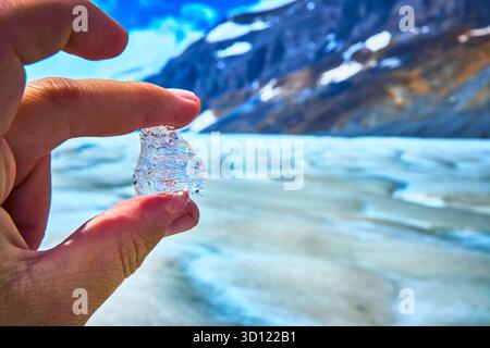 Gletschereis von Hand gegen Berg- und Schneelandschaft gehalten Stockfoto