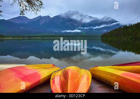 Farbenfrohe Kanus und Kajaks auf dem ruhigen See mit Misty Mountain Reflections Stockfoto