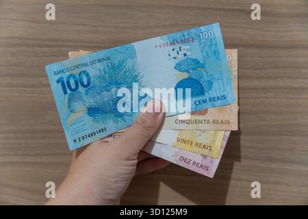 Frau Hand, die ein Bündel bunter brasilianischer Real Notes ergreift, darunter 100, 50, 20 und 10 Reais. Darstellung von Finanztransaktionen Stockfoto