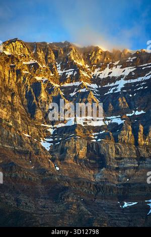 Goldenes Sonnenaufgangslicht auf der zerklüfteten Bergklippe mit Schnee und Wolken Stockfoto