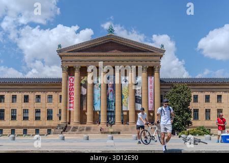 Ein Mann rennt vor einem großen Gebäude mit einem Banner mit der Aufschrift "Cassatt". Das Gebäude ist braun und hat viele Säulen. Es gibt noch andere Leute Stockfoto