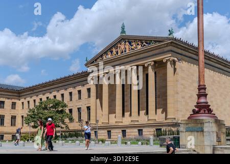 Eine Gruppe von Menschen läuft an einem großen Philadelphia Museum of Art mit einem hohen Stab davor vorbei. Das Gebäude hat ein klassisches Design und ist surr Stockfoto
