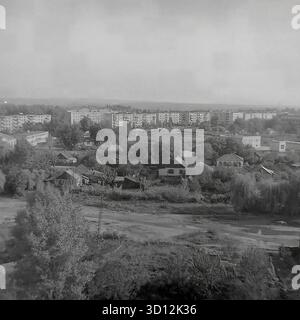 Ein Panoramablick aus der Höhe über das Wohnviertel Khimik in Sloviansk, 1970er-1980er Jahre Dieses Archivfoto aus der UdSSR, Ukrainische SSR, zeigt eine typische sowjetische Stadtlandschaft. Im Vordergrund befindet sich eine große Fläche flacher Privathäuser („chastnyy Sektor“) mit Gärten und unbefestigten Straßen, umgeben von Bäumen. Im Hintergrund stehen mehrstöckige Panelwohnungen („Panelka“), die den Hauptteil des „Schlafviertels“ bilden. Dies fängt den Kontrast der Stadtentwicklung ein. Ein wertvolles Dokument über das friedliche Leben im Donbass vor dem Krieg. Stockfoto