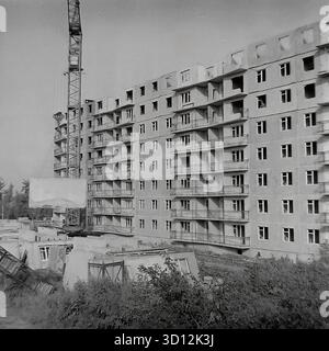 Ein großer Turmkran errichtet ein neues mehrstöckiges Wohnhaus („Panelka“) im Bezirk Khimik in Sloviansk, 1970er-1980er Jahre Dieses Archivfoto aus der UdSSR, Ukrainische SSR, zeigt ein typisches sowjetisches Wohnprojekt im Bau. Die Struktur des Hochhauses wird aus vorgefertigten Betonplatten montiert. Balkongeländer sind installiert, aber Fenster fehlen. Baukabinen sind im Vordergrund sichtbar. Dieses Bild fängt das Wesen der Stadtentwicklung ein. Ein wertvolles Dokument über das friedliche, konstruktive Leben im Donbass vor dem Krieg. Stockfoto