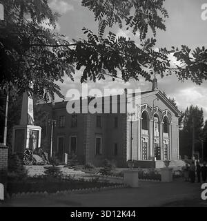 Der Kulturpalast der Eisenbahnarbeiter (DK ZHD) in Sloviansk, 1970er Jahre Dieses Archivfoto aus der UdSSR, der ukrainischen SSR, zeigt das beeindruckende Gebäude im neoklassizistischen stalinistischen Architekturstil. Daneben steht ein Denkmal aus dem Zweiten Weltkrieg mit einer Statue und Tafeln. Kulturpaläste waren zentrale Zentren für Kunst, Freizeit und Veranstaltungen in der Sowjetunion. Dieses Bild zeigt einen typischen sowjetischen öffentlichen Raum, der Kultur und historisches Gedächtnis verbindet. Ein wertvolles Dokument des friedlichen Bürgerlebens im Donbass vor dem Krieg. Stockfoto