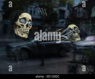 21. September 2025, Berlin: 21.09.2025, Berlin. In einem Schaufenster vor Halloween sind gruselige dekorative Skelette mit dunklen Kapuzen, Knochenhänden und Schädeln zu sehen. Ein Fahrzeug wird im Schaufenster reflektiert. Foto: Wolfram Steinberg/dpa Foto: Wolfram Steinberg/dpa Stockfoto
