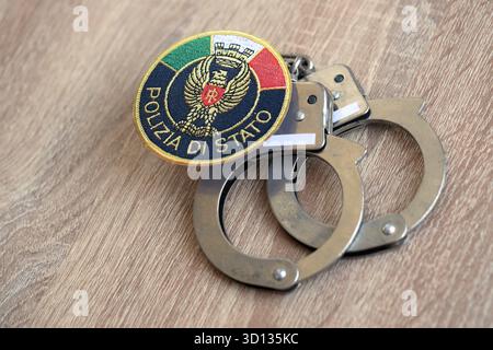 KIEW, UKRAINE - 6. SEPTEMBER 2025 Flicken der italienischen Staatspolizei und alte Handschellen aus Metall auf dem Tisch in Nahaufnahme Stockfoto
