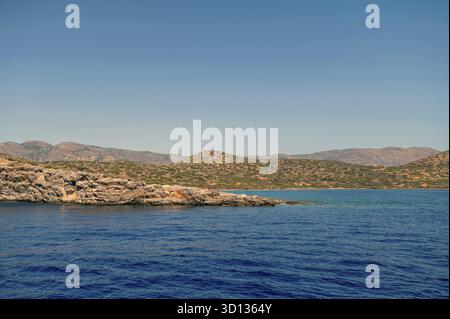 Wellen schlagen sanft gegen das felsige Ufer, während die Sonne auf Kreta hell scheint Stockfoto