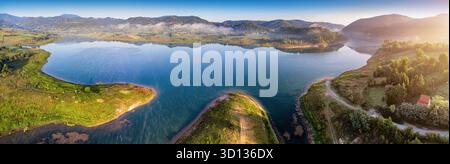 Panoramablick aus der Vogelperspektive mit einem ruhigen See, der Hügel und Himmel bei Sonnenaufgang reflektiert und eine ruhige, friedliche Landschaft schafft Stockfoto